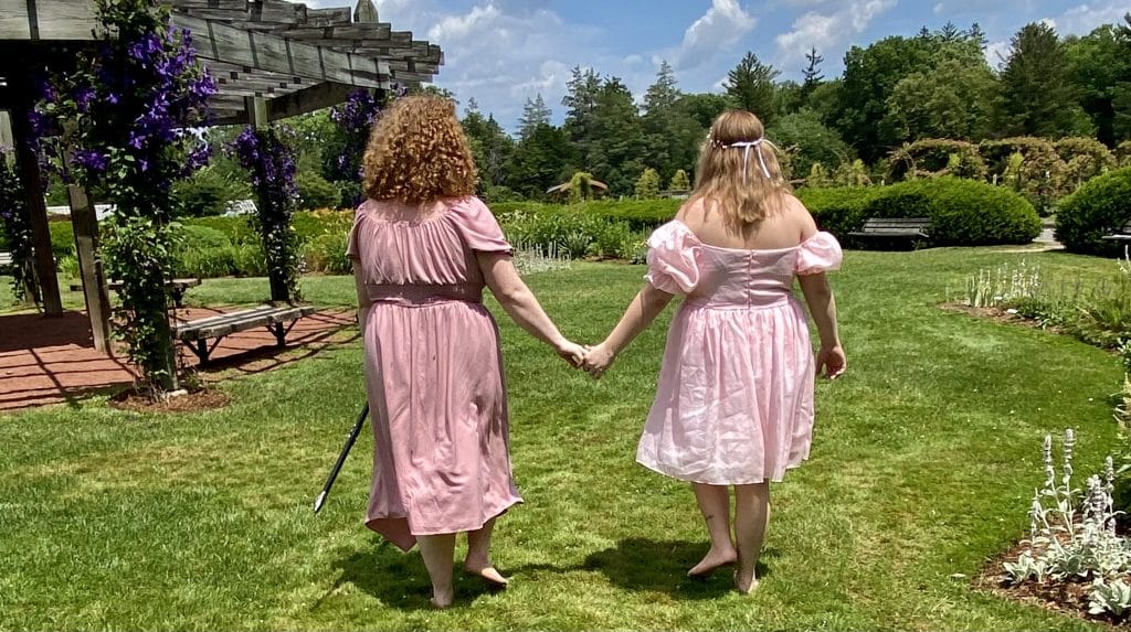 2 people in pink dresses walk while holding hands