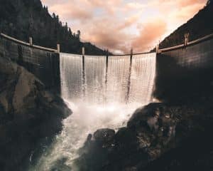 vertical image of a dam wiht four columns of water converging into a river over rocks