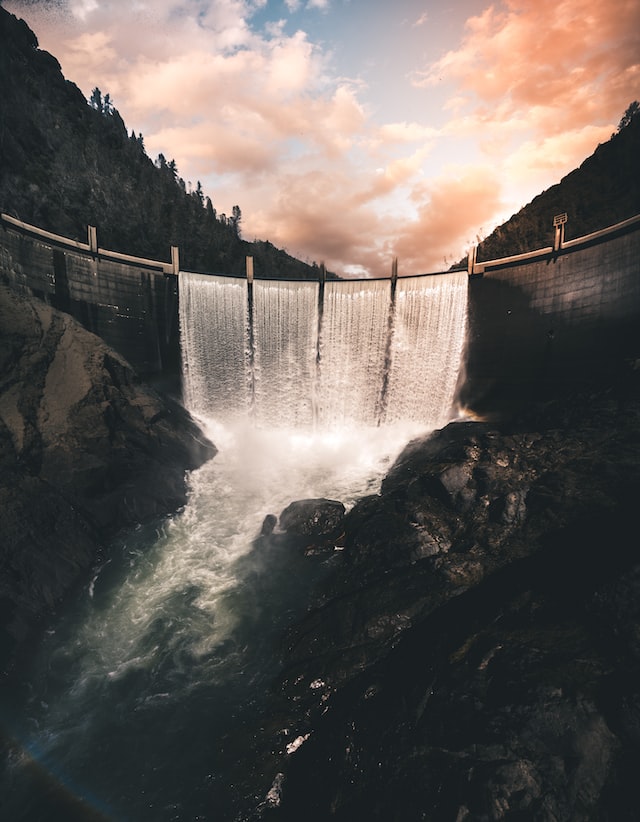 vertical image of a dam wiht four columns of water converging into a river over rocks