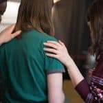 women viewed from behind with heads bowed and hands comfortingly placed on shoulders