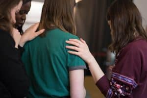 women viewed from behind with heads bowed and hands comfortingly placed on shoulders