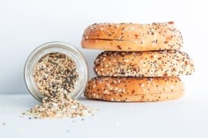 Three slices of everything bagels stacked on top of each other next to a glass jar of everything bagel spices with spice spilling out.