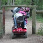 woman on scooter ducking under a wooden bar