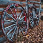 Two wagon wheels against log cabin.