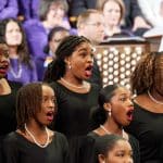 black women singing in a choir in the tabernacle with the organ in the background.