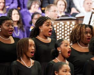 black women singing in a choir in the tabernacle with the organ in the background.