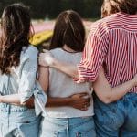 Three women with back to camera and arms around each other.