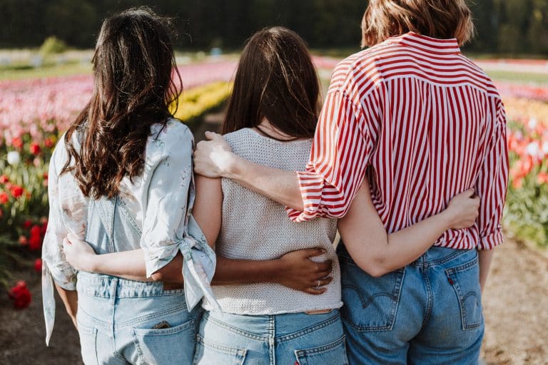 Three women with back to camera and arms around each other.