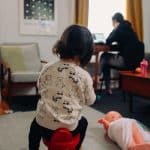 girl and white and black shirt sits on a red stool white watching her mother work on a laptop