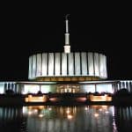 Provo Temple lit up at night, reflecting in fountain water.