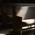 An empty wooden pew with a beam of light illuminating the seat.