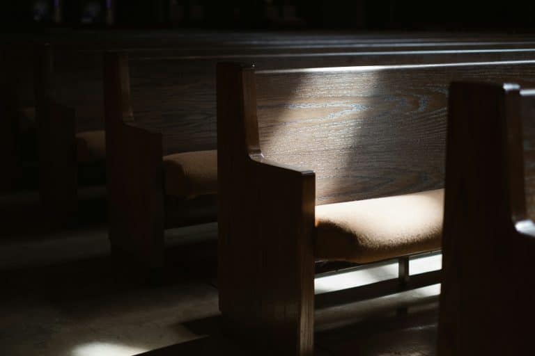 An empty wooden pew with a beam of light illuminating the seat.