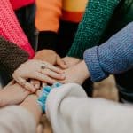 A group of people put their hands on top of each other to symbolize teamwork