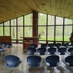 A picture of the chapel at pilgrimage. There are large windows on all sides looking out to a spring-green forest.