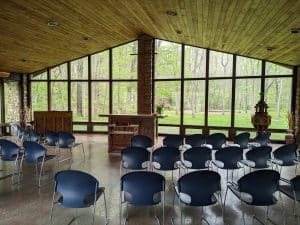 A picture of the chapel at pilgrimage. There are large windows on all sides looking out to a spring-green forest.