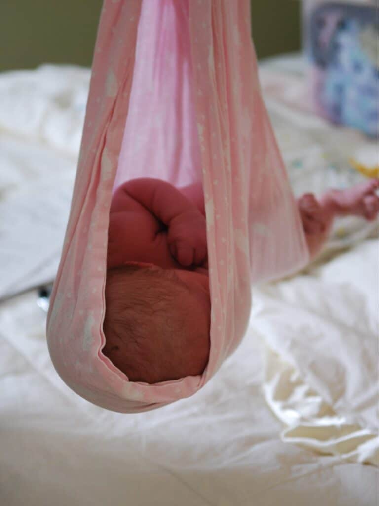 A newborn in a sling being weighed with a spring scale.