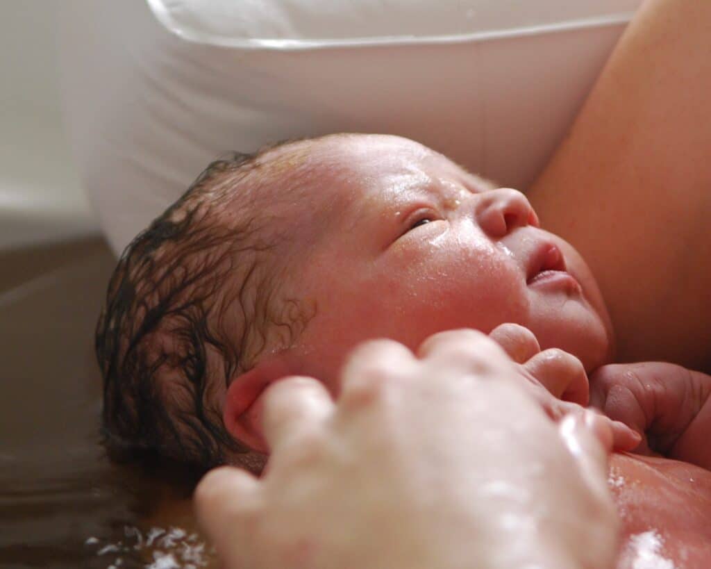 The face of a newborn in the bathtub with mom