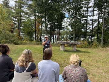 Nancy Dredge holding a microphone and speaking at the Exponent II retreat Quaker Meeting