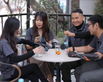 four people sitting at a table, each with a prosthetic arm