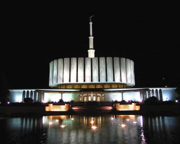 Provo Temple lit up at night, reflecting in fountain water.